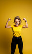 Portrait of a muscular and strong caucasian woman celebrating successes on yellow background,