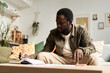 © Seventyfour - Portrait of adult African American man writing in notebook in sunlight and doing home finances, copy space
