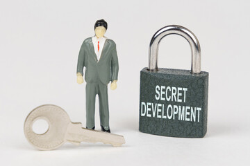 Poster - On a white surface there is a figurine of a businessman, a key and a lock with the inscription - Secret development