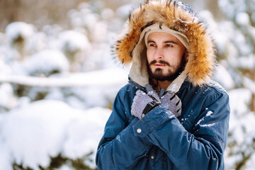 Wall Mural - Young stylish man in a snowy forest. Handsome man enjoying sunny winter weather. Concept of people, vacation.