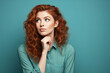 Attractive red-haired curly woman with a pensive uncertain expression on her face on a green background