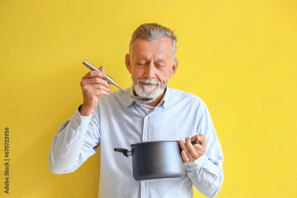 Mature man with ladle and cooking pot on yellow background