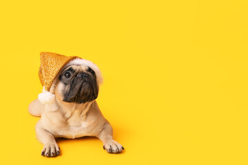 Cute pug dog in Santa hat lying on yellow background