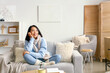© Pixel-Shot - Young Asian woman sitting on sofa at home