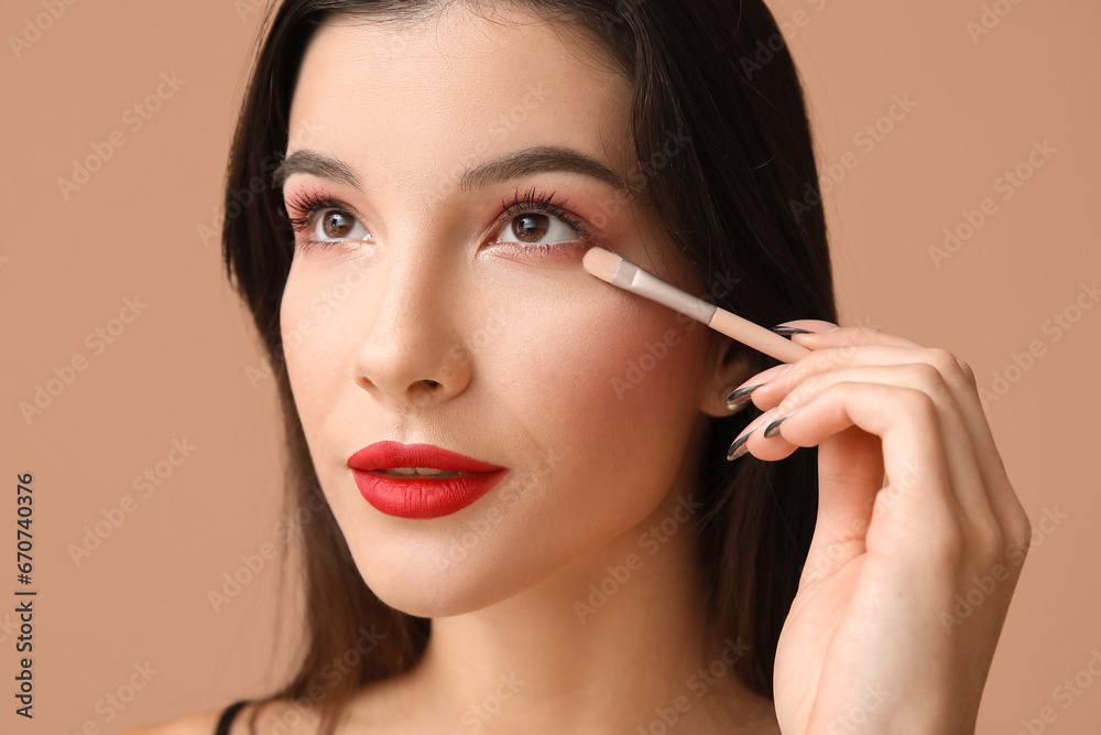 Beautiful young woman with brush applying eyeshadows on brown background