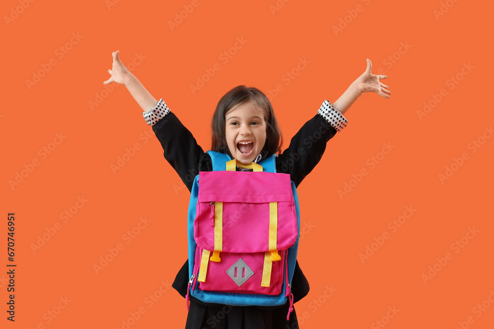 Happy little schoolgirl with backpack on orange background