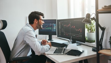 Poster - Great Happy young businessman or trader in formalwear looking at charts on computer screen in the office and smiling