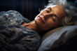 Close-up of a grey haired woman's sleeping face in darkened bedroom 