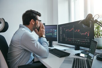 Fototapete - Working all day...Side view of tired young businessman or trader working with charts on computers at his modern office.