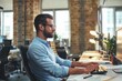 © Friends Stock - Side view of young and successful bearded man in eyeglasses and formal wear typing something on computer while sitting in the modern office