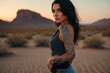 woman black hair, tattoos, light blue eyes in desert with sunset in the background, cinematographic , warm colors