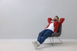 © New Africa - Handsome man relaxing in armchair near light grey wall indoors, space for text