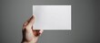 Hands holding a blank white business card on a gray background.