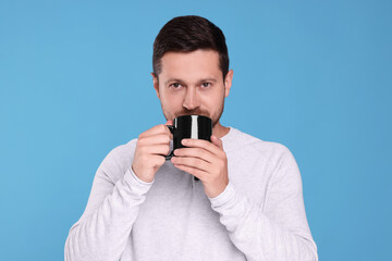 Poster - Portrait of man drinking from black mug on light blue background