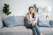 © Kawee - Asian beautiful woman sit on sofa and talk on mobile phone in house.