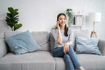 Wall Mural - Asian beautiful woman sit on sofa and talk on mobile phone in house. 