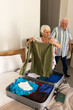 Happy caucasian senior couple packing suitcase in sunny bedroom at home
