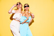 Two young beautiful smiling brunette hipster female in trendy summer clothes. Sexy carefree women posing near yellow wall in studio. Positive models having fun. Cheerful and happy. In sunglasses