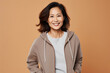 Smiling Asian woman posing in a beige hoodie on a beige background. Athleisure style