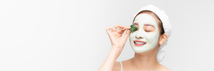 Wall Mural - A woman with white nourishing mask on face and green leaf in hand, white banner isolated.