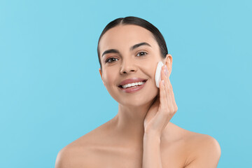 Canvas Print - Beautiful woman removing makeup with cotton pad on light blue background