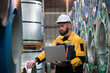 © amorn - Male factory worker using laptop computer inspecting quality rolls of galvanized or metal sheet in in aluminum material warehouse. Male worker working in warehouse during distribution process