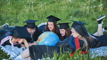 Wall Mural - Graduate students in black robes study a globe on the grass.