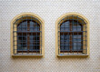 Two arched wooden windows protected by metal grilles. Set in a stone window band and white brick wall