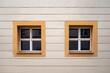 Two small wooden white windows on the facade of the old building, the windows are square with a yellow band around them