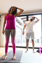 Happy biracial couple stretching practicing yoga and smiling in sunny room at home