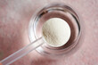Collagen powder in a plastic scoop with a glass of water