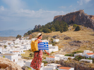 Wall Mural - Young traveling woman with national greek flag enjoying view of Lindos. Travel to Greece, Mediterranean islands outside tourist season.