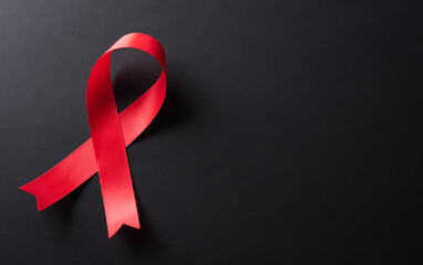 Closeup red ribbon HIV, world AIDS day awareness ribbon on black background. Healthcare and medicine concept.