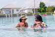 © Ekkasit A Siam - African woman and Hispanic, close friends two multiethnic people standing in water Eating watermelon in pond and chatting happily Wear swimsuit Wear hat and sunglasses in pool on hot sunny days.
