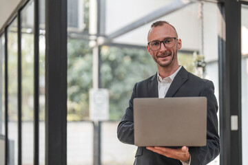 Wall Mural - Successful businessman standing in modern office Use a laptop computer Organization or financial manager who is successful in planning investment projects