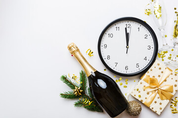 New year celebration concept with a bottle of champagne and two glasses toasting. Christmas gift box, alarm clock and fir tree branch on colored table. Top view Copy space