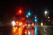 Verkehr mit Autos auf nasser Straße mit Lichterspiegelung vor Ampel in Großstadt bei regen in der Nacht im Herbst