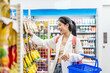 Young asian woman buy snacks and dried fruits at store, She stand against shelves and look to product details. Then search for required goods on racks, pick it up and put into shopping cart