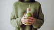 Winter seasonal smoothie drink detox. Female in woolen sweater holding bottle of green smoothie or juice making heart shape with her hands. Clean eating, weight loss, healthy dieting food concept 