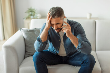 man engaging in difficult conversation over cellphone sitting at home