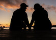 closeup of silhouettes of man and woman, husband and wife, married couple, facing each other and holding hands on boat dock with lake and scenic sunset in background