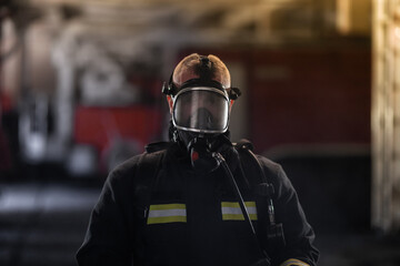 Firefighter wearing full equipment and emergency rescue equipment wiht oxygen mask Fire trucks in the background.