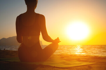 girl does yoga and meditates in lotus position on the beach. silhouette of a young woman by the sea at dawn, healthy lifestyle concept, view from the back