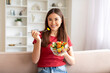 © Prostock-studio - Asian woman eating vegetable salad while sitting on couch in living room