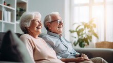 Happy Laughing Elderly Retired Couple Sitting On The Couch At Home And Watching TV Shows Together, Family Spending Time Together