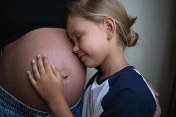 little cute daughter hugging pregnant mother at home