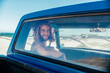 © Marko Geber - Young man with wavy hair smiling from his blue car at the beach