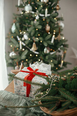 Wall Mural - Stylish wrapped christmas gifts, rustic basket with fir branches and modern decorations against festive decorated tree in scandinavian room. Merry Christmas and Happy holidays!