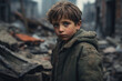Portrait of Caucasian child boy with a sad face with eyes full of tears and fear in his eyes standing between ruined buildings in destroyed city. War conflict, earthquake concept