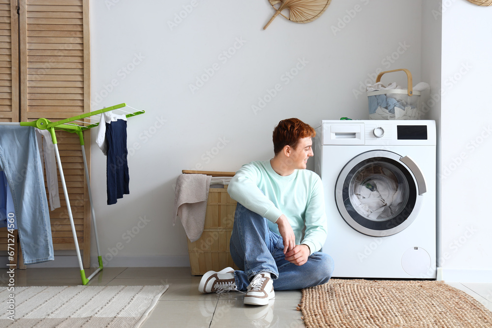 Young man sitting near washing machine at home